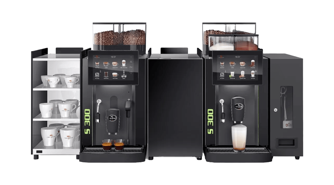 Treehouse coffee. Commercial coffee machine with touchscreen controls. Two dispensers are brewing, with one dispensing coffee into a mug. Coffee beans are visible on top. A side compartment holds stacks of disposable cups and has a storage cabinet.