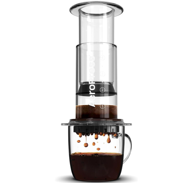 Badger & Dodo. The Aeropress Coffee Maker-Clear Colours presses rich, dark coffee into a glass mug, with vibrant colors highlighting each drip below.