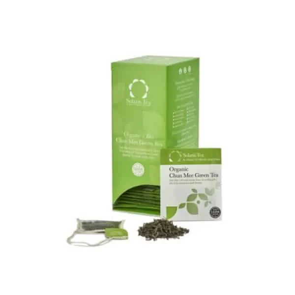 Badger and Dodo Coffee Roasters: A box of Solaris Organic Chun Mee Green Tea with vibrant green packaging, adorned with eco-friendly symbols. Next to it sits a tea sachet, alongside a pile of loose tea leaves and a tea bag, inviting you to enjoy an authentic and sustainable brew.