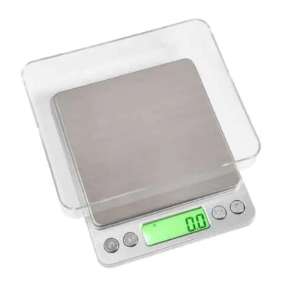 Badger and Dodo Coffee Roasters: Introducing the Envy Series Miniscale 3000g: a sleek kitchen scale with a stainless steel surface, green backlit display at zero, and clear cover. It features three intuitive buttons and handles up to 3000g precisely.